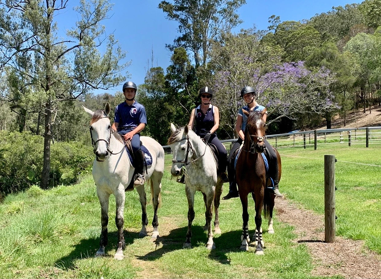Three riders on the trail under a jacaranda