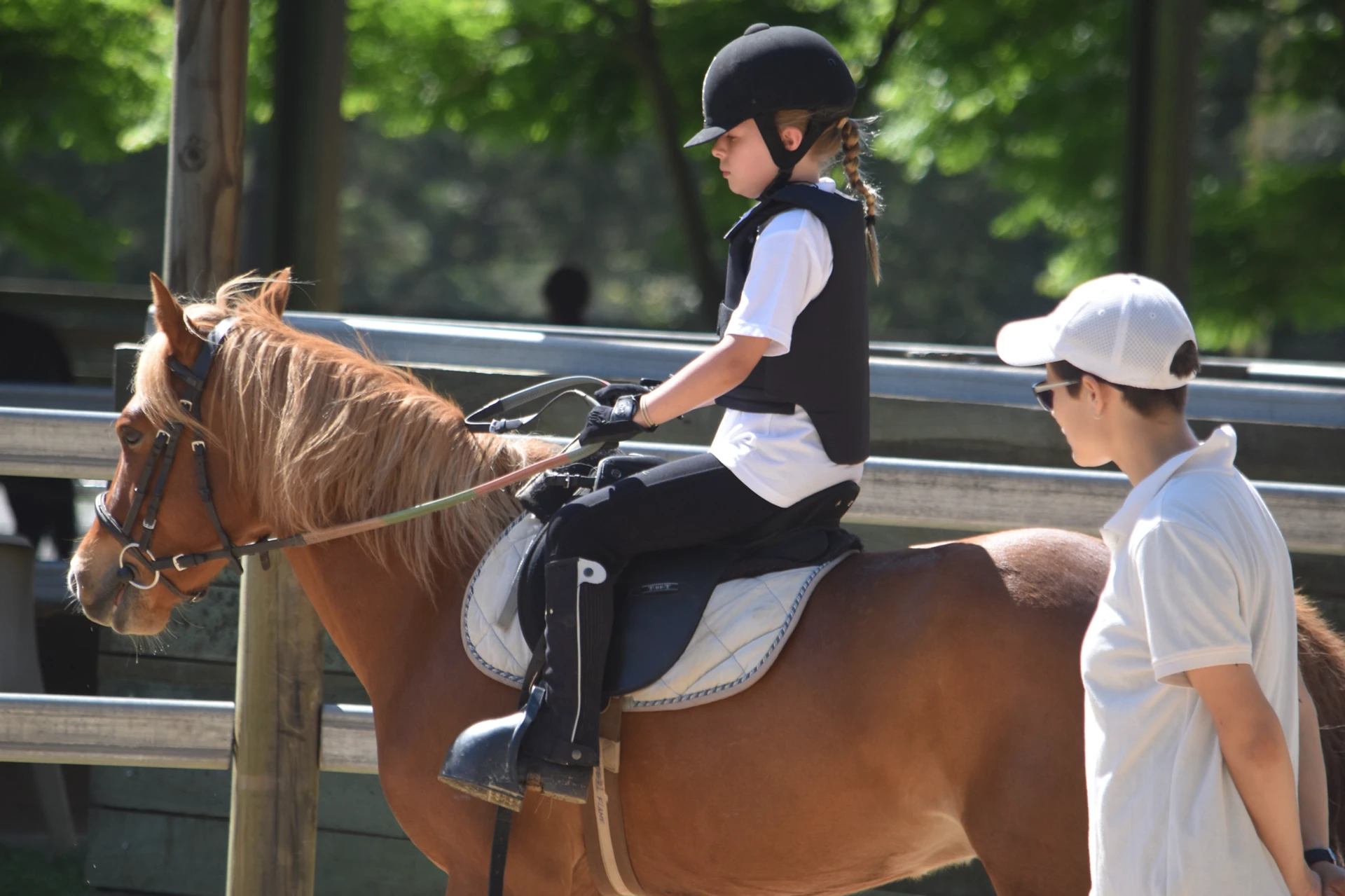 A young rider on a chestnut pony with her coach